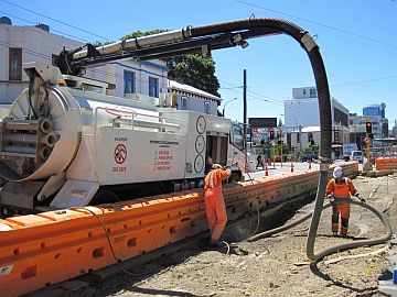 Workers using a hydrovac machine to carefully expose pipes so they can be moved.